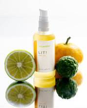 Bottle of Desavery LIT! body oil with citrus fruits on a white background